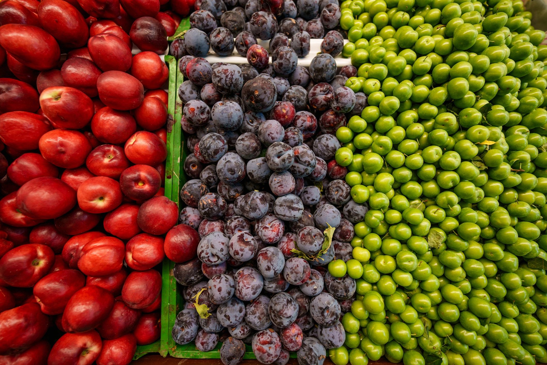 Fresh peaches, purple plums, and green plums at a produce stand